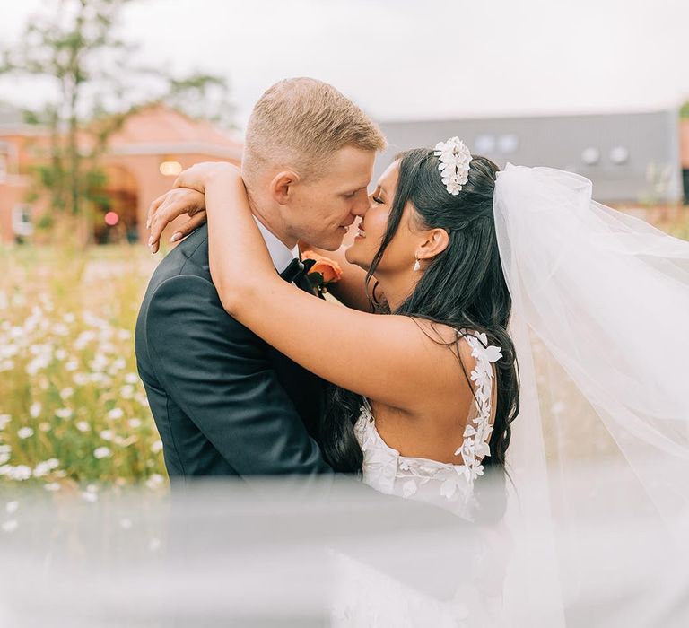 Cute couple wedding photo of the bride and groom sharing a kiss with the veil blowing in the wind 