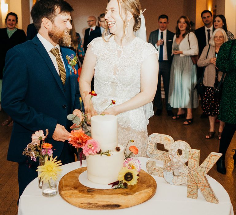 The bride and groom cut their two tier white iced wedding cake with seasonal wedding flowers 