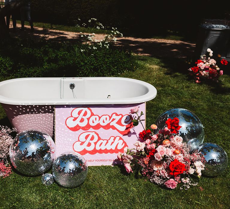 Booze bath wedding drinks station for alcoholic beverages with pink and red flowers and disco balls 