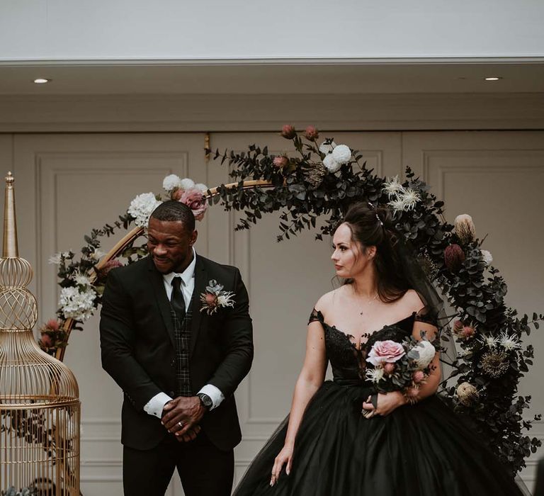 Bride in black strapless wedding dress standing with groom in front of floral moongate decoration