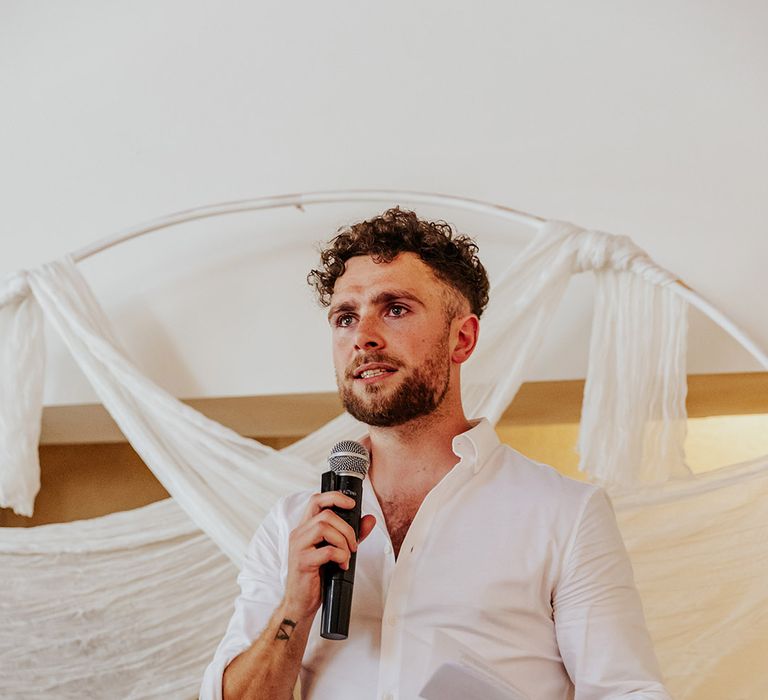 Groom in white shirt stands with microphone to read out his wedding speech 