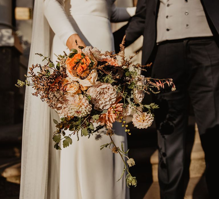 Bride carrying orange and cream wedding bouquet with the groom in an autumnal wedding 