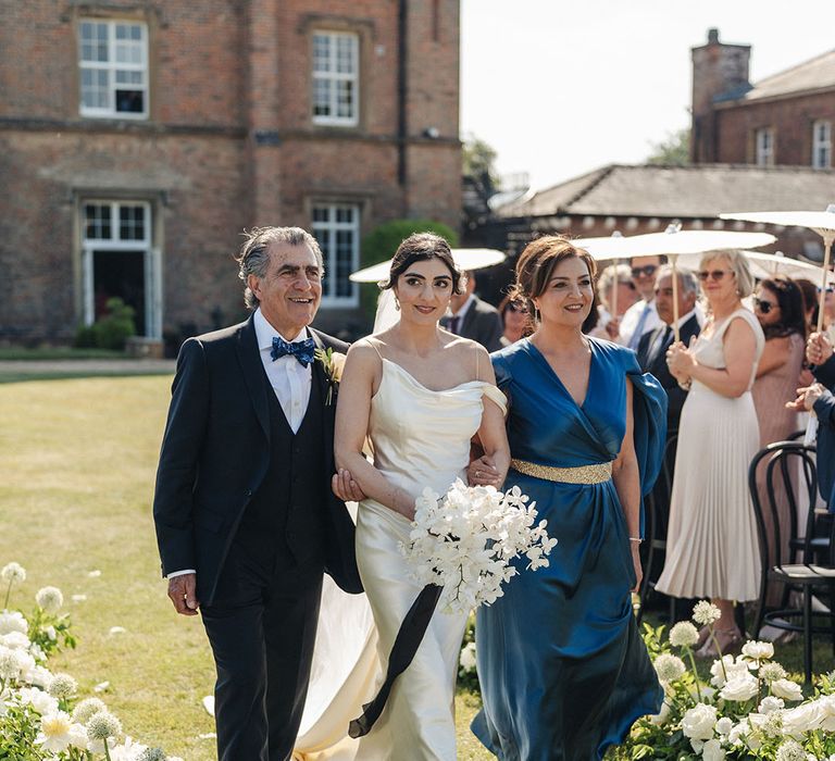 Bride walking down the aisle with both of her parents in blue outfits 