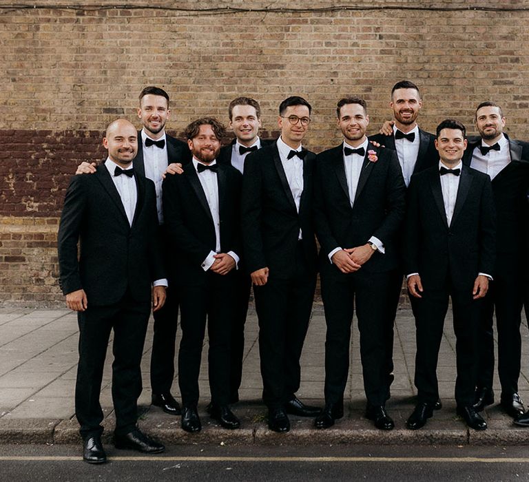 The groom and groomsmen stand wearing black tuxedos 