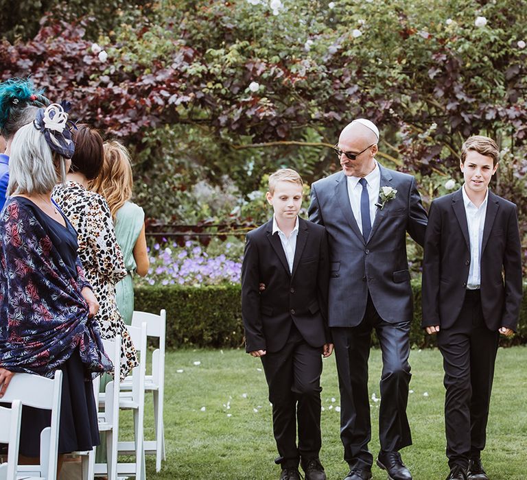 Two page boys in dark navy wedding suits waking down the aisle at outdoor wedding ceremony in Braxted Park 