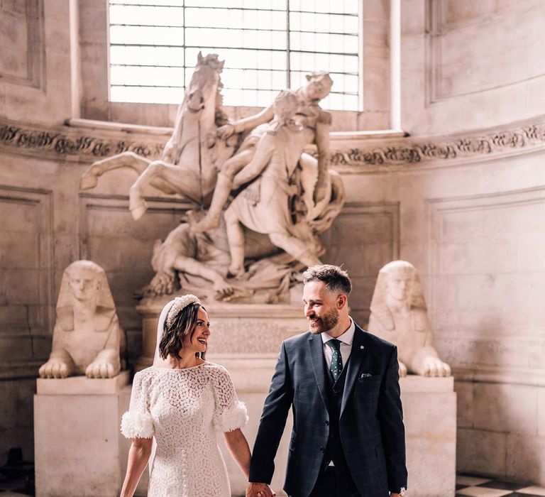 Bride in floral wedding dress walking with the groom in three piece navy wedding suit at St. Paul's Cathedral 