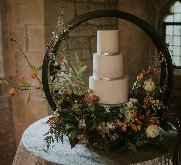 White wedding cake with silver leaf decor on a hoop cake stand decorated with autumn flowers 