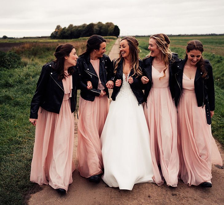 Bridal party wearing peach bridesmaid dresses and leather jackets with the bride wearing a cold shoulder wedding dress