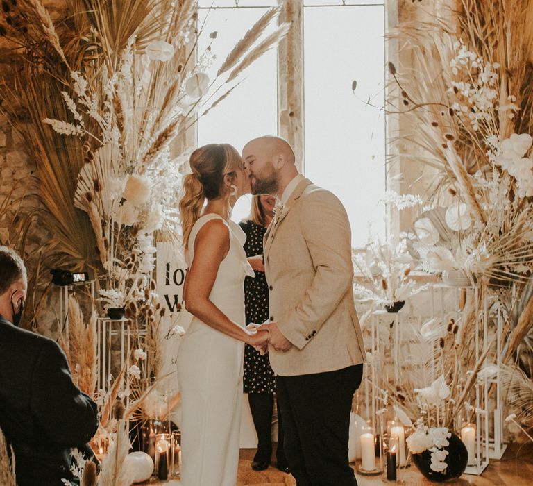 Bride and groom kissing at intimate wedding ceremony with dried flowers wedding decor 