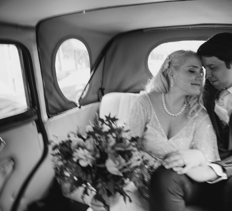 Bride & groom sit together in vintage car on wedding day 