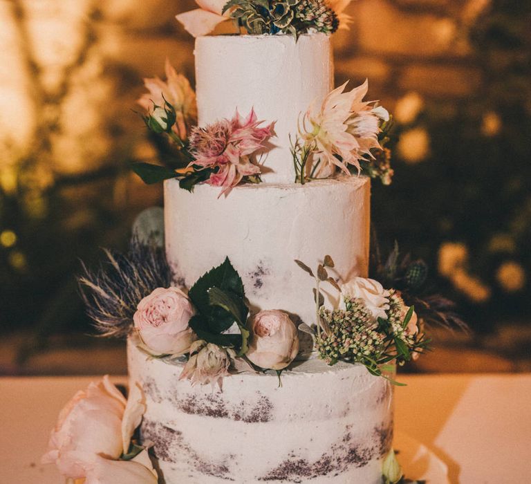 Three tier white naked wedding cake decorated with pink and purple flowers