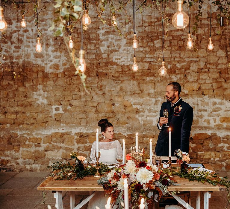 Bride & groom sit together with brick wall background and hanging lights