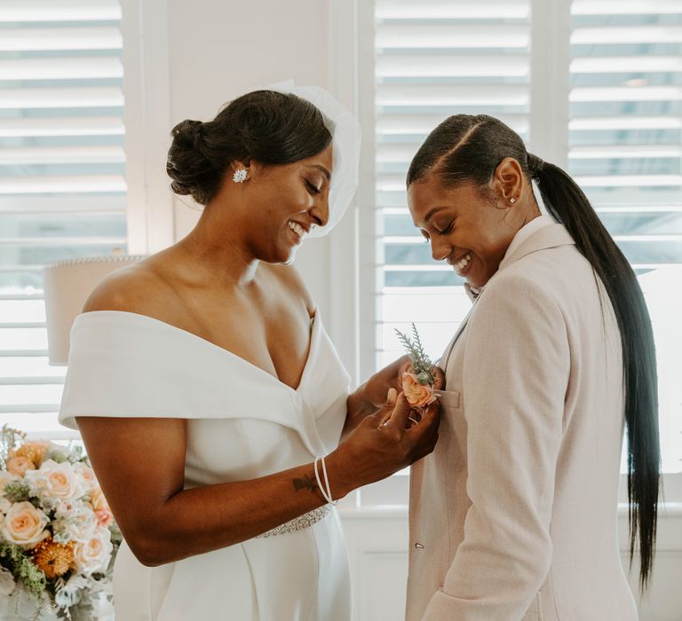 Black bride in an off the shoulder jumpsuit with jewel belt detail putting on her best person's buttonhole