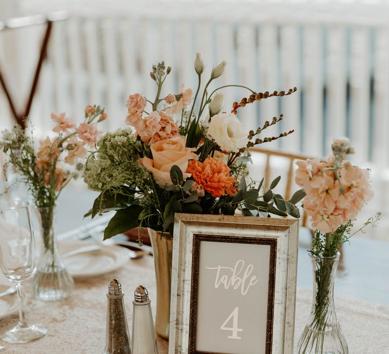 Gold foil table number sign in a frame surrounded by colourful wedding flowers 