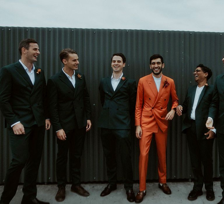 Groomsmen portrait with groom in a double breasted orange suit and groomsmen in teal suits. 