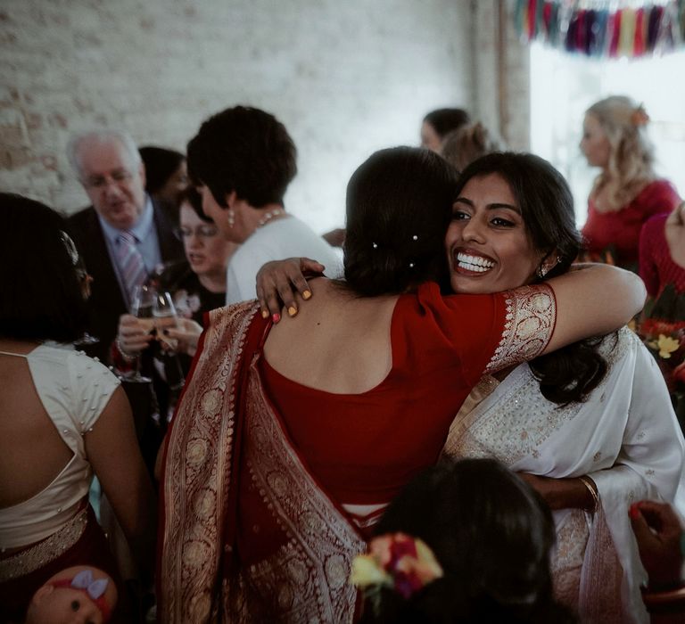 Wedding guest in a read and gold sari embracing the bride 