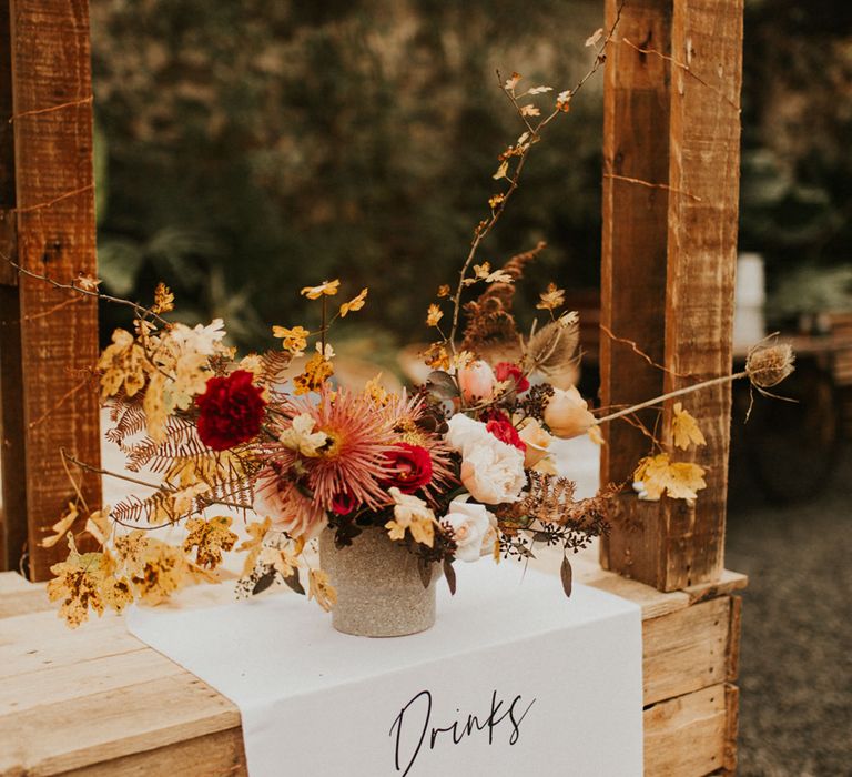 Fabric drinks menu hanging over the wooden bar with an orange, red and yellow floral arrangement 