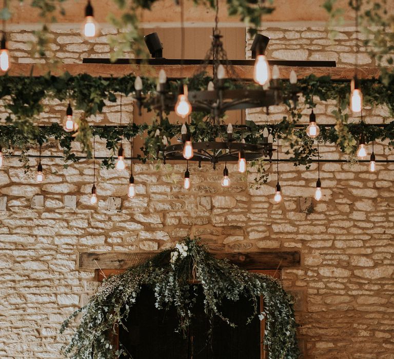 Ivy foliage wedding arch in stone barn with hanging pendant lightbulbs and ivy foliage at Caswell House wedding