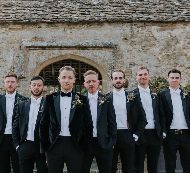 Groom in black velvet Hugo Boss suit and bow tie standing with groomsmen in black Moss Bros suits and white bow ties