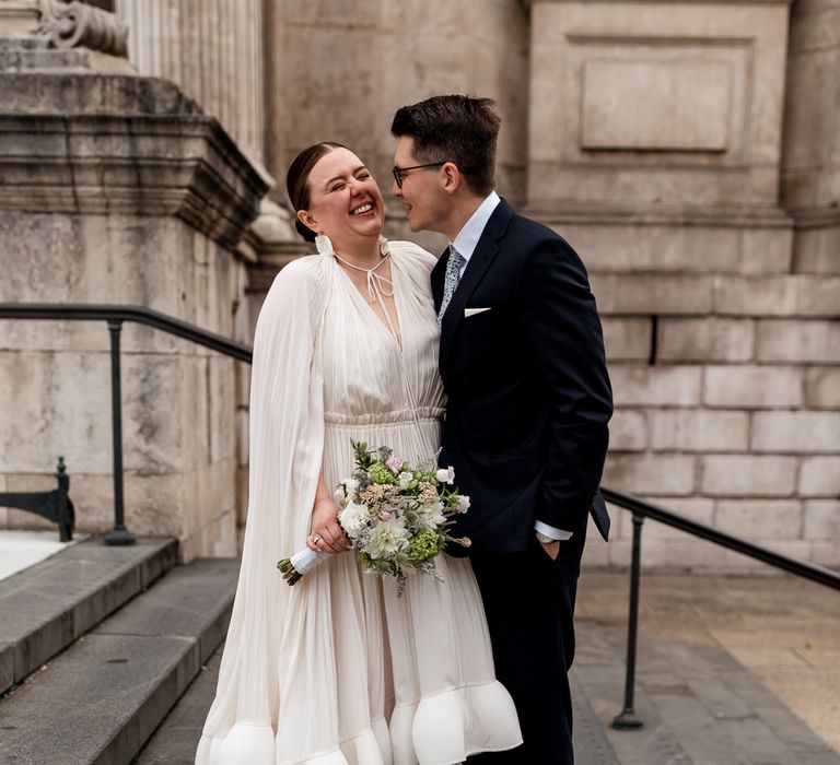 Groom in a navy suit making his bride laughing in a Lanvin wedding dress with ruffle hem cape