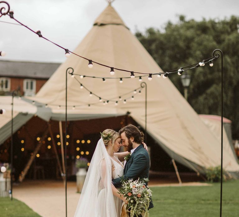 Bride & groom stand outside wedding tipi outdoors 