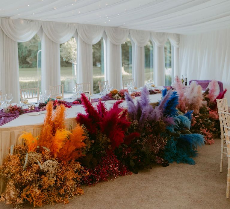 Orange, pink, purple and blue pampas grass floral installation at top table of wedding breakfast 