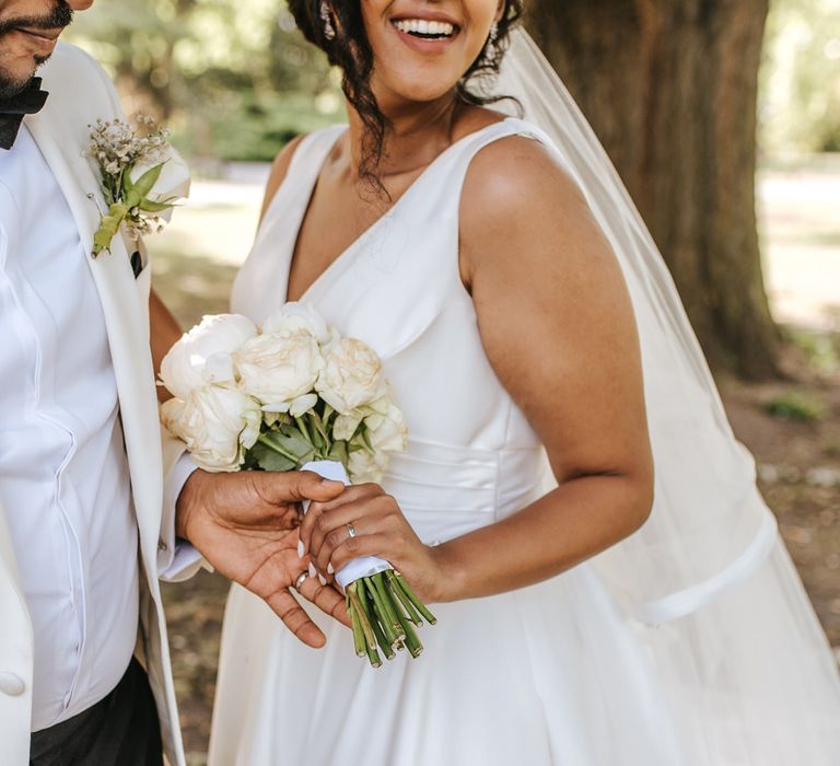 Groom in a white tuxedo holding his brides hand looking at her wedding ring 