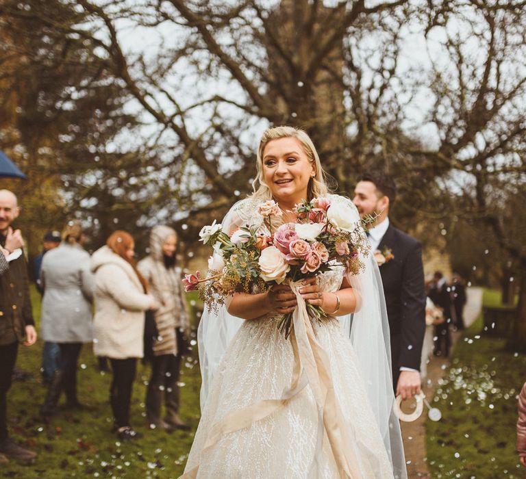 Bride in a princess wedding dress by Enzoani and bespoke bridal cape holding a blush pink wedding bouquet 