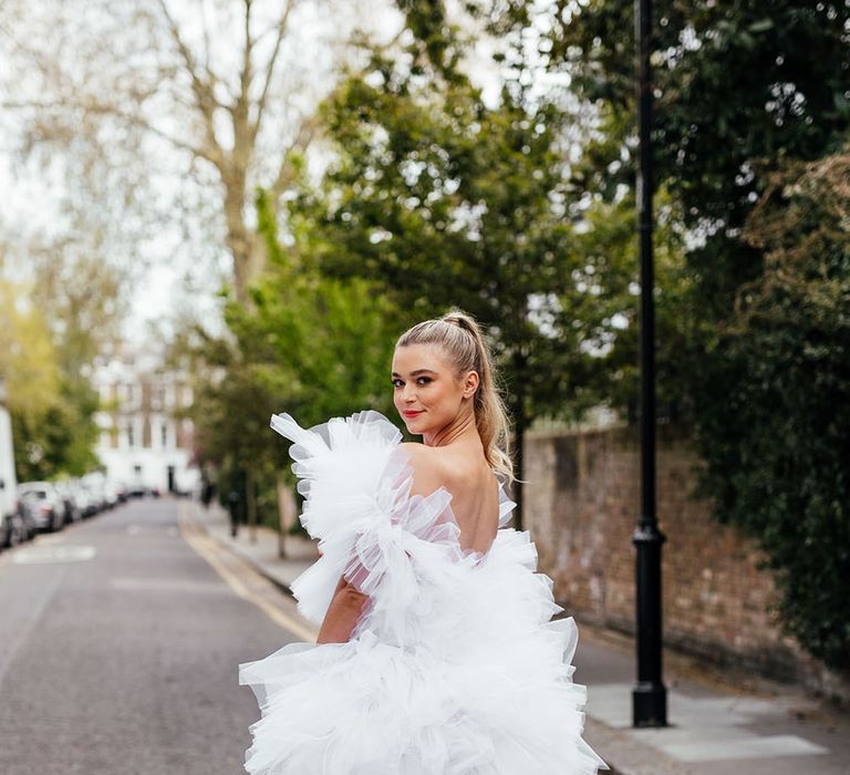 Stylish bride in a short layered tulle wedding dress and platform shoes with sleek back ponytail 