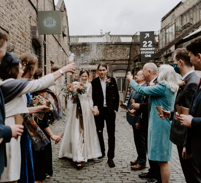 Bride and groom walking through hackney street as their wedding guests shower them in confetti 