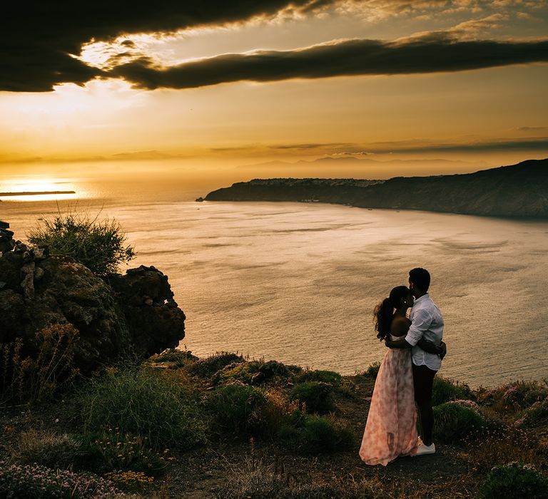 Bride & groom stand beside the sea during sunset in Santorini 