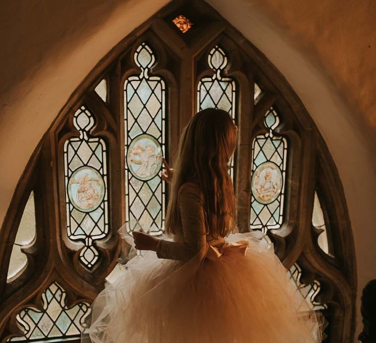 Flower girl looking out a stain glass window in a tutu