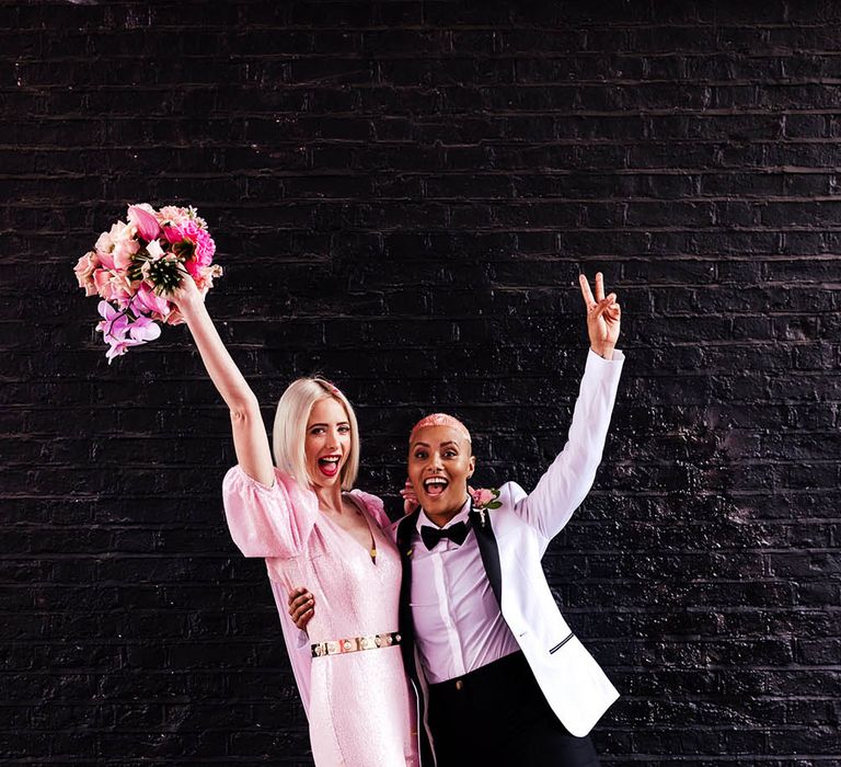 Alternative bride and bride photo with brides in a pink jumpsuit and white tuxedo jacket 