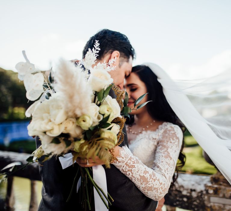 Groom holds out brides classic bouquet as her veil blows in the wind