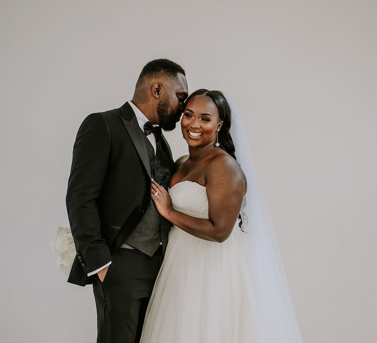 Bride & groom embrace for couples portraits after wedding ceremony in front of white wall