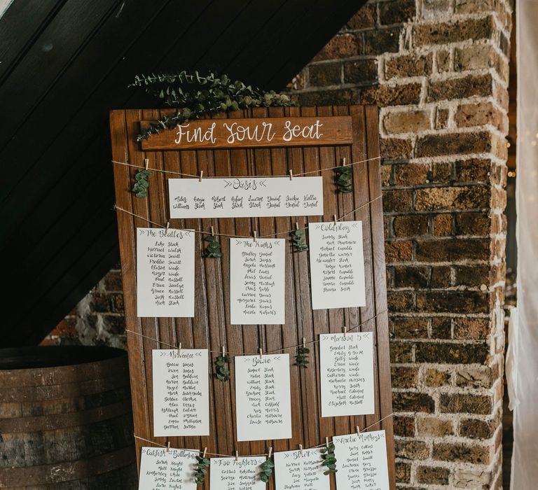 Wooden board complete with seating plan on white stationery and decorated with green foliage