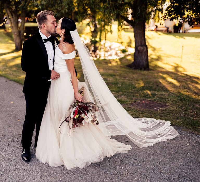 Bride and groom share a kiss at Lea Manor Farm wedding with dried flower installation