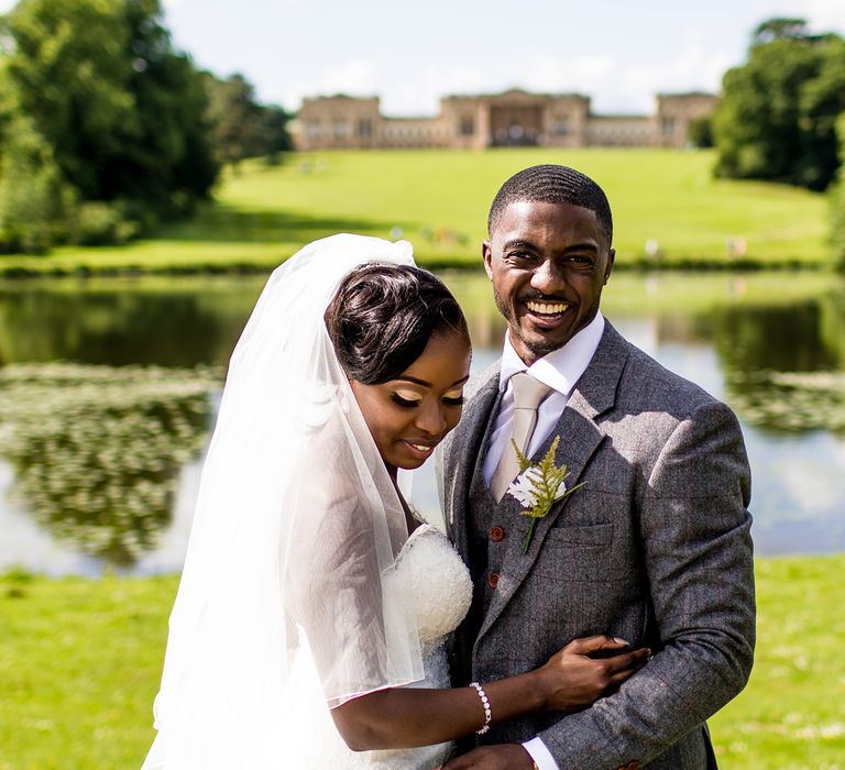 Black groom in a grey tweed wool wedding suit laughing and embracing his bride at their classic country wedding 