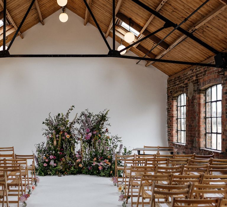 Wedding ceremony room at Loft Studios London with exposed wooden ceiling, wooden chairs, white walls and multicoloured floral installation 