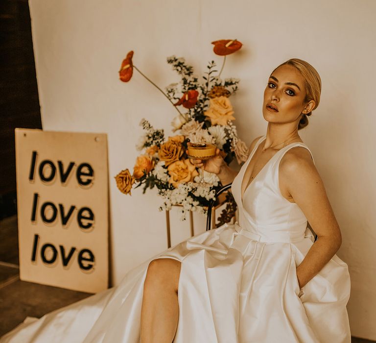 Bride in a taffeta Jesus Peiro wedding dress with front split and metallic gold shoes sitting on a chair in Churdshall Barn 