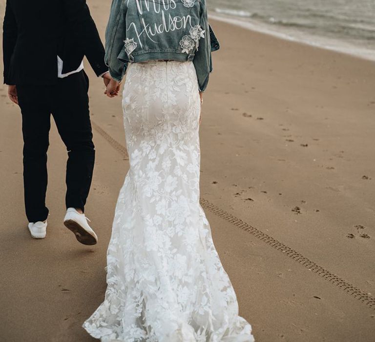 Bride on a beach in a light blue denim jacket with with personalised detail on the back 