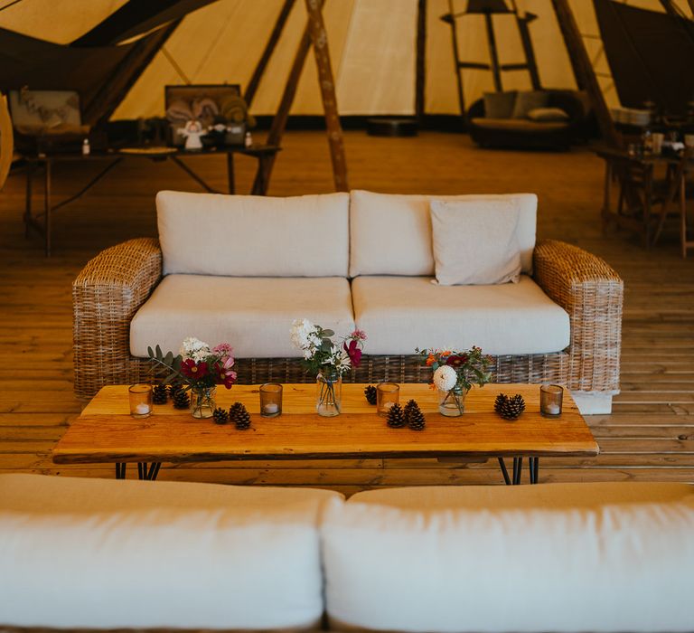 Two rattan sofas with white sofa cushions and wooden coffee table laid with florals, candles and pinecones for late summer wedding at Wellington Wood Norfolk