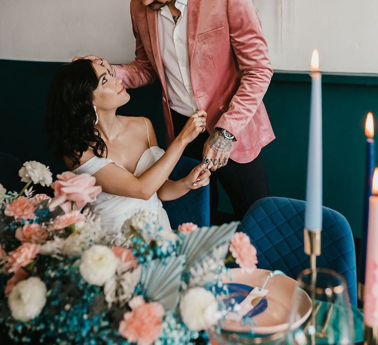 Groom in a pink velvet jacket standing next to his bride in a cold shoulder wedding dress at their stylish pink and teal wedding reception 