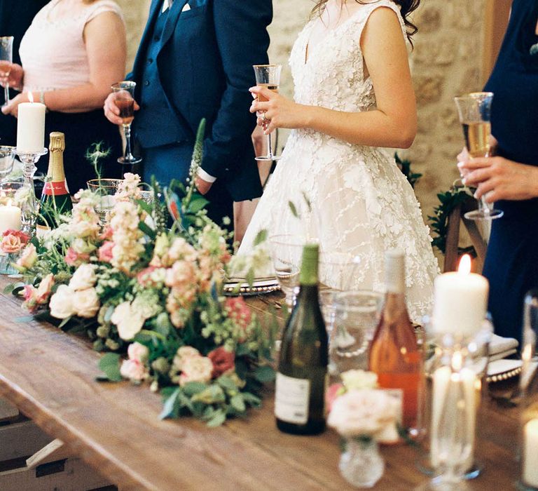 Groom in a navy suit and bride in an appliqué wedding dress with flower in her loosely pinned her standing during the wedding reception speeches