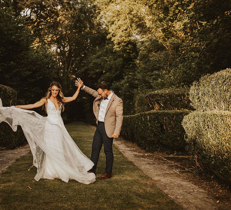 Bride lifts up her wedding gown outdoors as her groom holds her hand