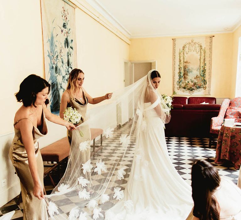 Bride wears Halfpenny London veil complete with floral embellishments as bridesmaids help with veil