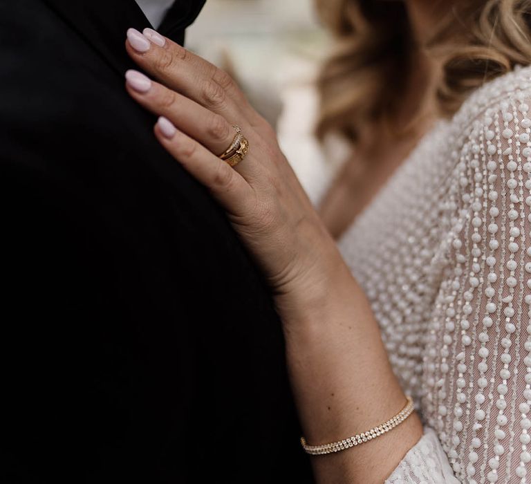 Bride in an embellished wedding dress with pink wedding nail and diamond tennis bracelet embracing her groom 