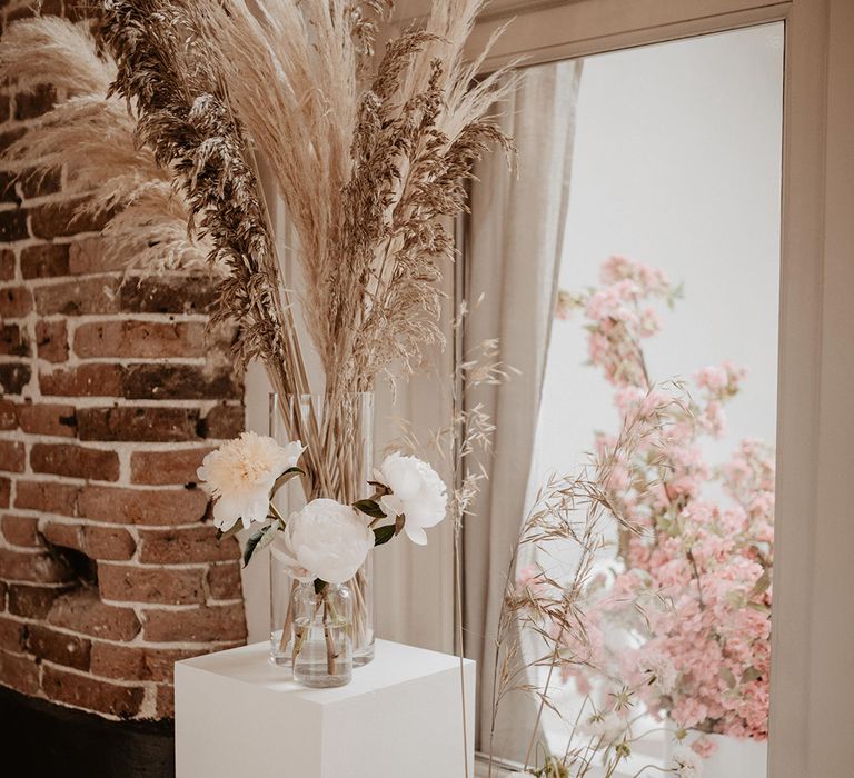 Large dried floral bouquets in clear vase complete with pampas grass next to window