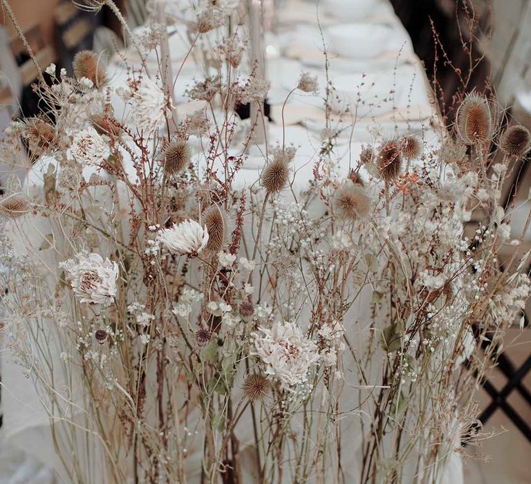 Tall dried flower stems in a wooden stand at the end of the wedding reception table 