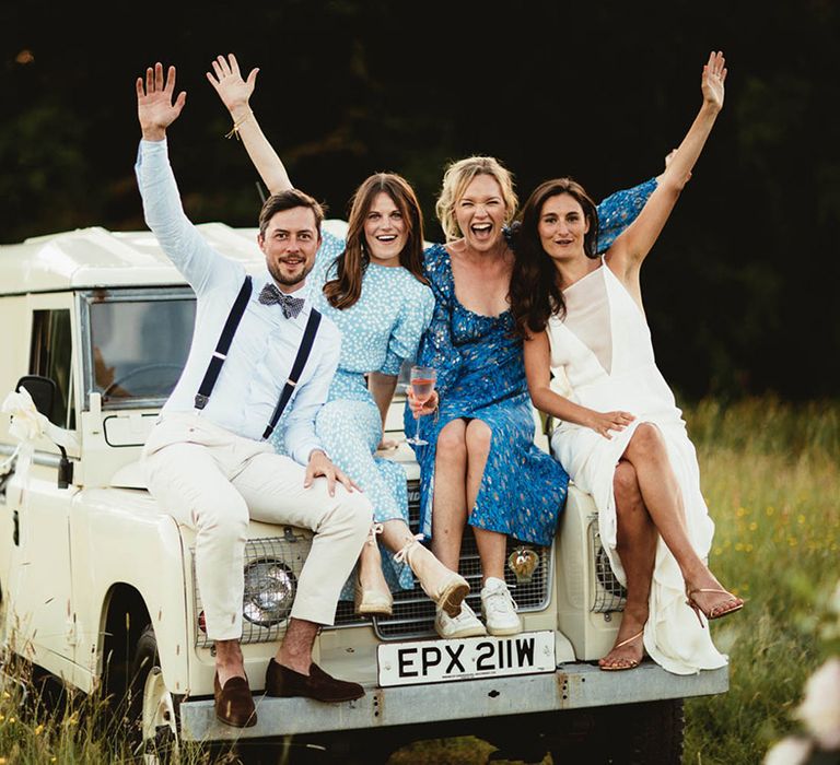 Bride & groom sit on Defender with friends on their wedding day